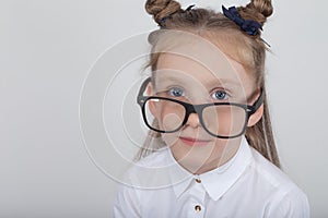 Happy little girl portrait, wearing white blouse and black frame eyeglasses, standing against white wooden background. Back to sch