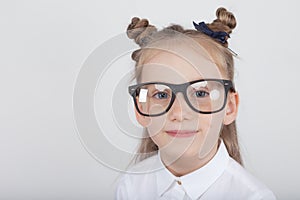 Happy little girl portrait, wearing white blouse and black frame eyeglasses, standing against white wooden background. Back to sch