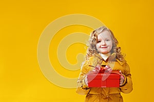 Happy little girl preschooler in a winter jacket is holding a box with a gift. The concept of giving and receiving gifts.