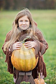 Happy little girl on pumpkin patch on cold autumn day, with a lot of pumpkins for halloween or thanksgiving