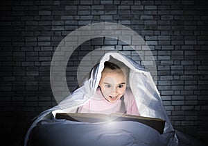 Happy little girl reading book in bed