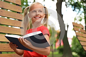 Happy little girl reading book in park