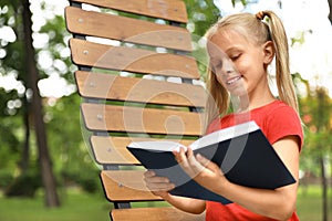 Happy little girl reading book in park