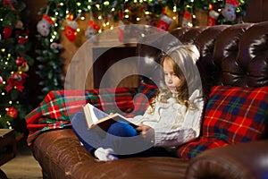 Happy little girl reading a story book by on the couch in a cozy