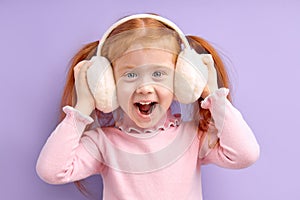 Happy little girl with red hair stand wearing wireless headphones, enjoy listening to music