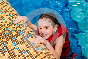 Happy little girl in a red vest swimming in the pool of the water park. Child learns to swim. teaching a child to swim