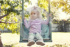 Happy little girl rides on a swing in a beautiful summer garden. Active summer holidays for children.