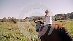 A happy little girl riding a horse in the nature on a sunny day. She is smiling. Slow mo, back view