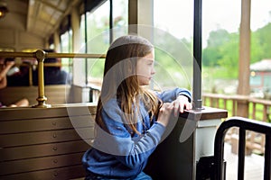 Happy little girl riding a train in a theme park or funfair