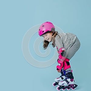 Happy little girl in roller skates with pink protective gear over blue