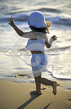 Happy little girl running along the sea on the beach