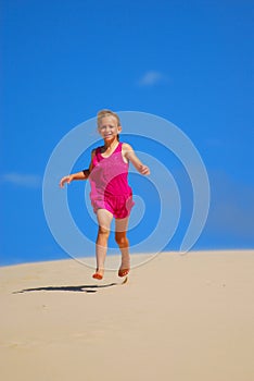 Happy little girl running down sand dunes