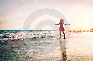 Happy little girl running inside water spreading her hands up on the beach - Baby having fun making splashing in the sea