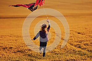 Happy little girl running with kite in hands on the beautiful field