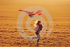 Happy little girl running with kite in hands on the beautiful field