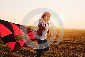 Happy little girl running with kite in hands on the beautiful field at sunrishe time