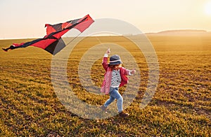 Happy little girl running with kite in hands on the beautiful field at sunrishe time