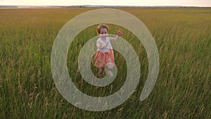 Happy little girl runs across a green field with outstretched arms. The child enjoys the fresh air laughs and claps his