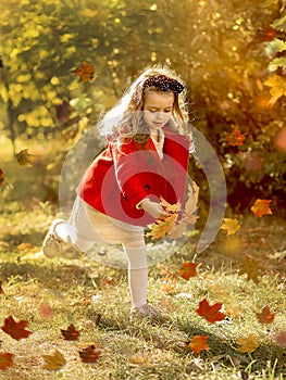 A happy little girl runs in the park with autumn leaves in a bright red coat and gray knitted skirt. Childhood. Active children.