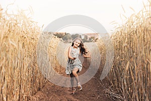 A happy little girl runs through a wheat field in the summer on a sunny day. Summertime. Summer vacation. Happy childhood.