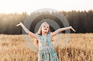 A happy little girl runs through a wheat field in the summer on a sunny day. Summertime. Summer vacation. Happy childhood.