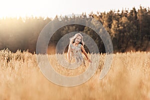 A happy little girl runs through a wheat field in the summer on a sunny day. Summertime. Summer vacation. Happy childhood.