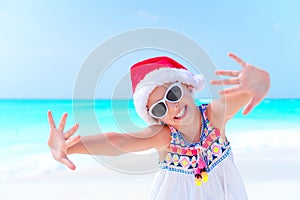 Happy little girl in Santa hat on Christmas beach vacation