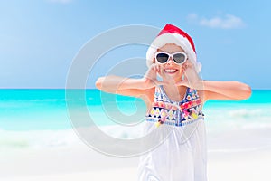 Happy little girl in Santa hat during Christmas beach vacation have a lot of fun