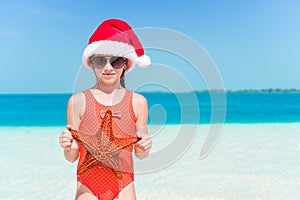 Happy little girl in Santa hat during Christmas beach vacation have a lot of fun