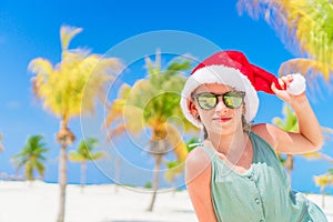 Happy little girl in Santa hat during Christmas beach vacation have a lot of fun