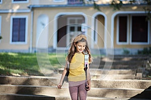 Happy little girl with school bag walking in front of school