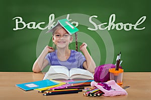 Happy little girl in the school bench, behind Back To School sign on the blackboard