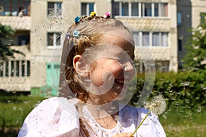 Happy little girl of seven years among flying dandelion seeds