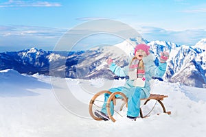 Happy little girl sit on sledge in mountains