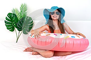 Happy little girl sits on a bed in a hat. Imitation of Holidays during a pandemic. Domestic tourism
