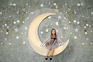 Happy Little girl sits on a yellow moon. Sweet dreams.