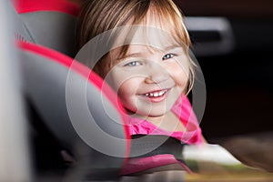 Happy little girl sitting in baby car seat