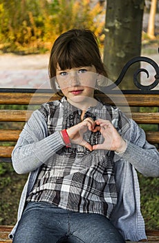 Happy little girl sitting on the bench and make handly sign of heart