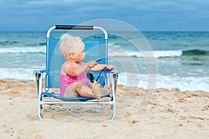 Happy little girl sitting on chair at beach