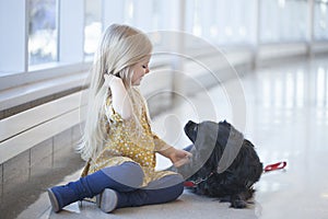 Happy little girl sitting on floor and playing with black dog