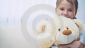 Happy little girl sitting on the sofa, hugging a big teddy-bear.