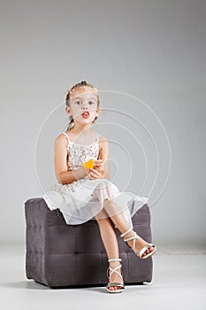 Happy little girl sitting on a stool in studio, eating crisps