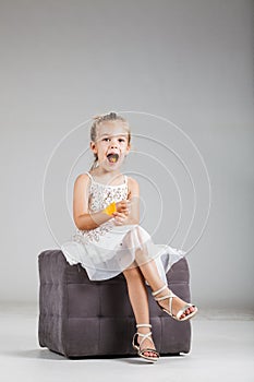 Happy little girl sitting on a stool in studio, eating crisps