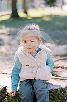 Happy little girl sitting on stump in sunny park