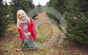 Happy little girl sitting on toboggan among fir trees