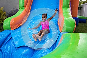 Happy little girl sliding down an inflatable bounce house