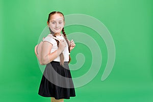 Happy little girl smiling aand holding backpack while standing in studio on green background