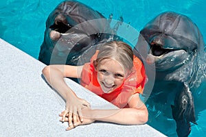 Happy Little Girl Smiling with two Dolphins in Swimming Pool