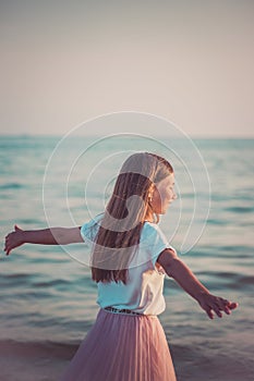 Happy little girl is spinning and dancing on the beach on a Sunny day.