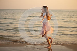 Happy little girl is spinning and dancing on the beach on a Sunny day.